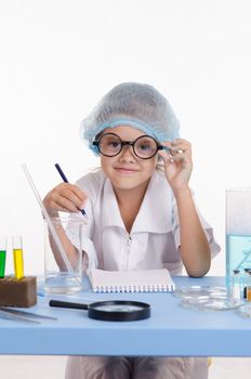 Chemist girl sitting at the table with the reagents in chemistry class and puts experiments