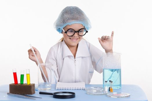 Chemist girl sitting at the table with the reagents in chemistry class and puts experiments
