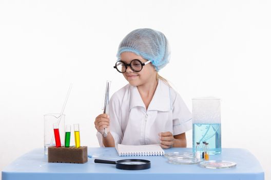 Chemist girl sitting at the table with the reagents in chemistry class and puts experiments