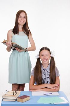 Teacher standing at desk behind which sits a diligent student