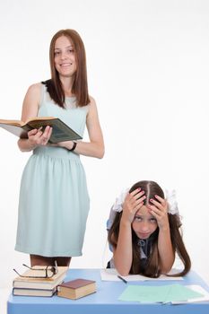Teacher standing at desk behind which sits a tired student