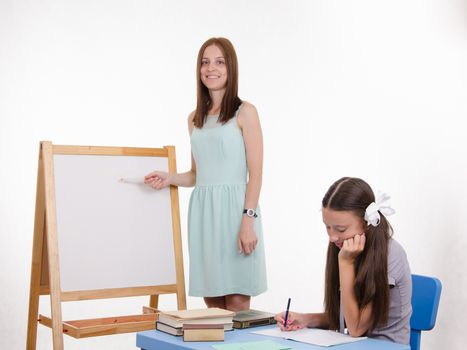 The teacher stands at the blackboard, a student sitting at a desk and listening to the teacher