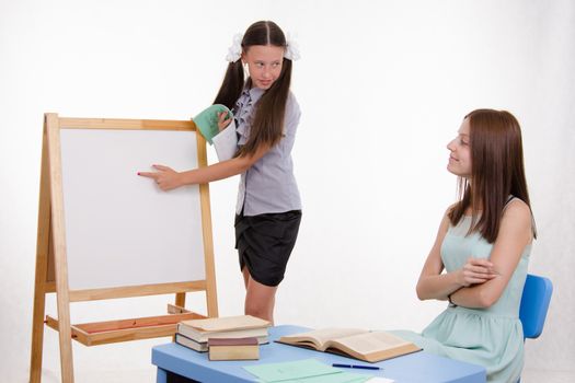 Pupil stands at the blackboard, the teacher sits at his desk and listens to the student