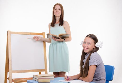 The teacher stands at the blackboard, a student sitting at a desk and listening to the teacher