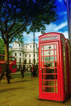 LONDON - SEPTEMBER 27, 2013: Tourists walk in front of a red phone booth. The city is visited by more than 30 million people every year