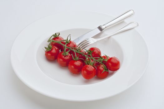 cherry tomatoes on a plate with fork and knife isolated on white