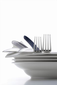 closeup of silverware on pile of plates with white cloth