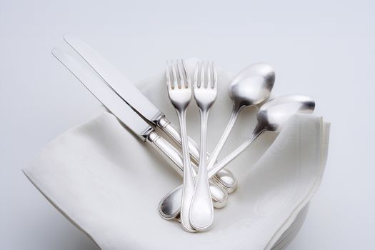 closeup of silverware on pile of plates with white cloth
