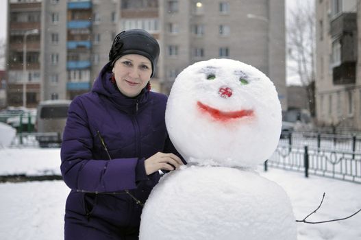 The woman near a snowman in the yard of the house