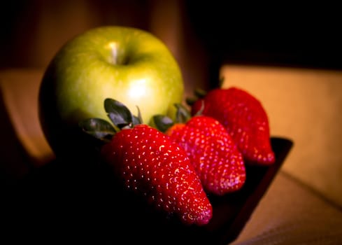 Warm and intimate background with green apple in the background and three strawberries on black background. Digital format.