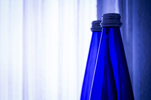Blue glass bottle of water against white background, space for advertising.
