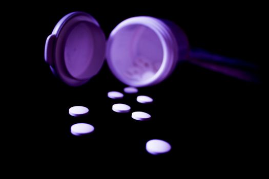 White pills floating out of its open container on black background.