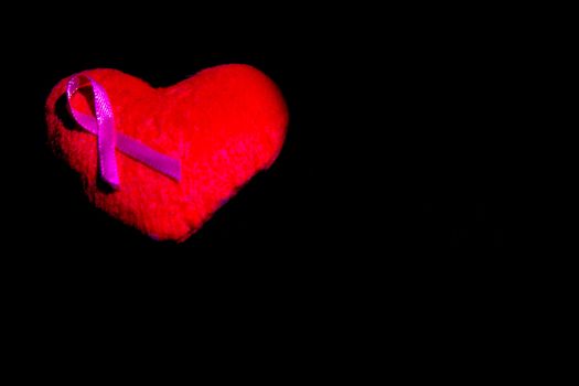 Red heart with pink ribbon on black background.