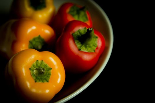 Colorful peppers in white bowl on black background.