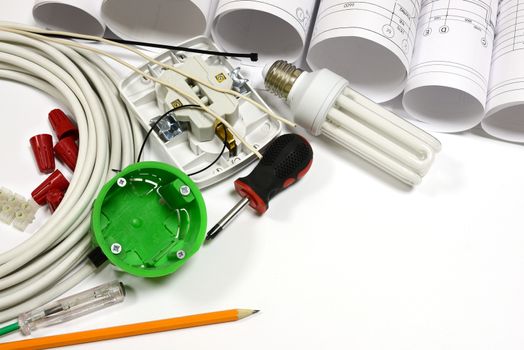 Drawing rolls, wall socket, socket box, power cable, screwdriver, lamp, test pen, pencil, fasteners, wire connectors, terminal block and wires on white surface