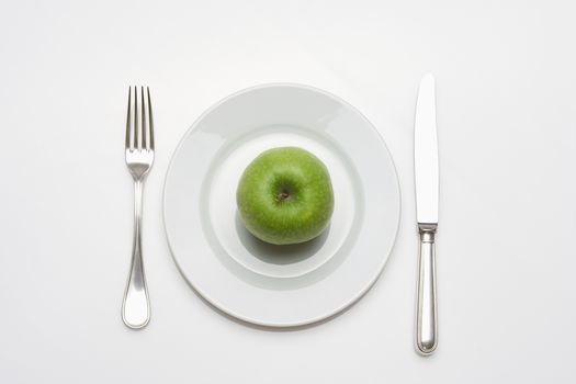 diet - green aplle on a white plate with knife and fork