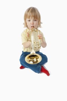 boy with long blond hair playing with toy trumpet