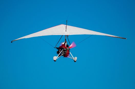 Ultralight aircraft from behind as it is taking of in to the blue skys, with pilot infront, and passanger right behind.