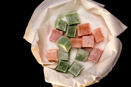 Several pieces of Turkish Delight in a bowl lined with white tissue paper all on a black background.