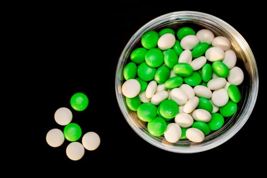 A glass bowl filled with white and green mints viewed from above while on a black background and five mints out, next to the bowl.