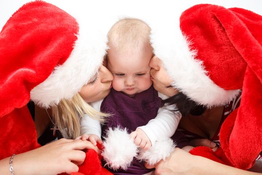 mother and her aunt with santa hat kissing infant baby on white background