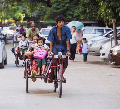 YANGON, MYANMAR - NOVEMBER 13, 2014: Children being taken to school on cyclos. The cyclo is an important mode of transportation in the Myanmar capital, where motorbikes are forbidden.