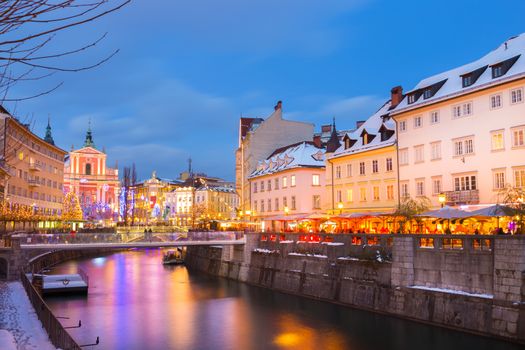View of lively river Ljubljanica bank and Tromostovje in old city center decorated with Christmas lights at dusk. Ljubljana, Slovenia, Europe. 