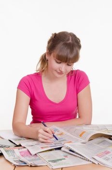 A young girl sits at a table with a pile of newspapers, encyclopedias and a laptop