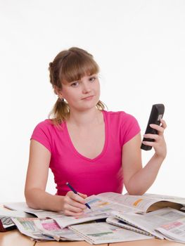 A young girl sits at a table with a pile of newspapers, encyclopedias and a laptop