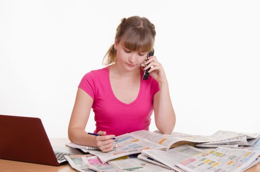 A young girl sits at a table with a pile of newspapers, encyclopedias and a laptop