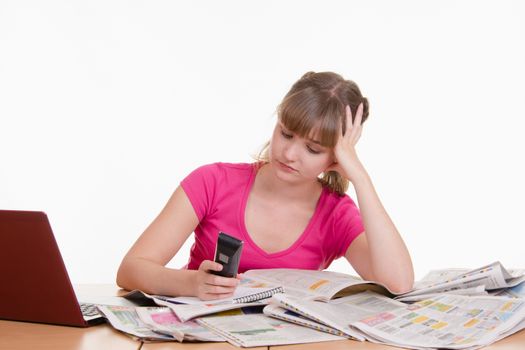A young girl sits at a table with a pile of newspapers, encyclopedias and a laptop