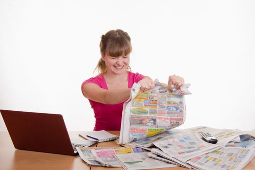 A young girl sits at a table with a pile of newspapers, encyclopedias and a laptop