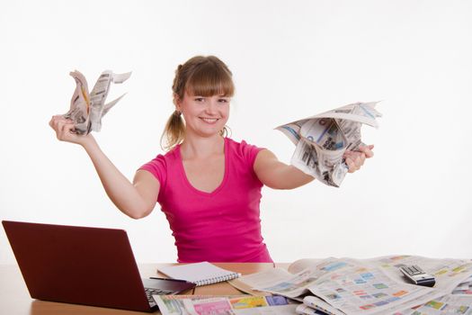A young girl sits at a table with a pile of newspapers, encyclopedias and a laptop