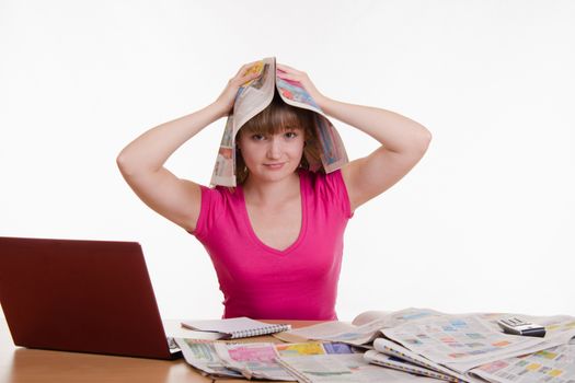A young girl sits at a table with a pile of newspapers, encyclopedias and a laptop