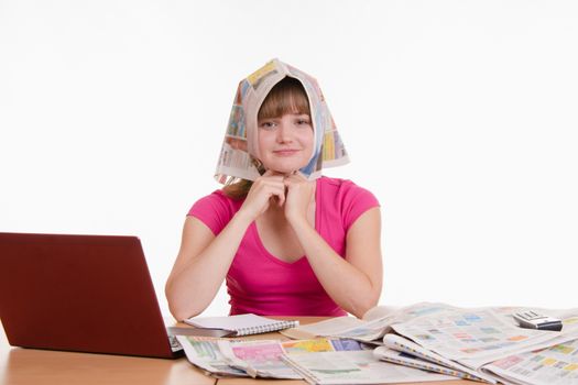 A young girl sits at a table with a pile of newspapers, encyclopedias and a laptop