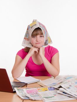 A young girl sits at a table with a pile of newspapers, encyclopedias and a laptop