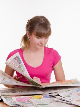 A young girl sits at a table with a pile of newspapers, encyclopedias and a laptop