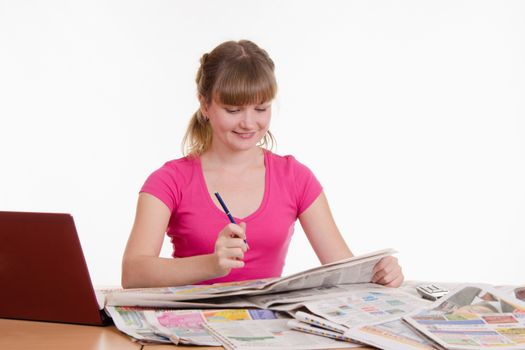 A young girl sits at a table with a pile of newspapers, encyclopedias and a laptop