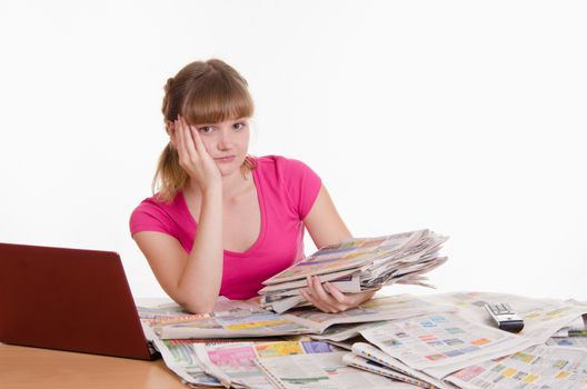 A young girl sits at a table with a pile of newspapers, encyclopedias and a laptop