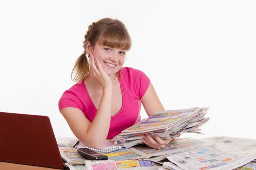 A young girl sits at a table with a pile of newspapers, encyclopedias and a laptop