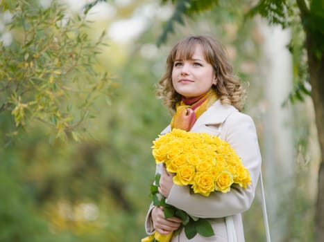 Young cute girl with a bouquet of yellow roses in autumn cool weather