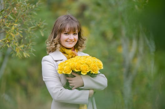 Young cute girl with a bouquet of yellow roses in autumn cool weather