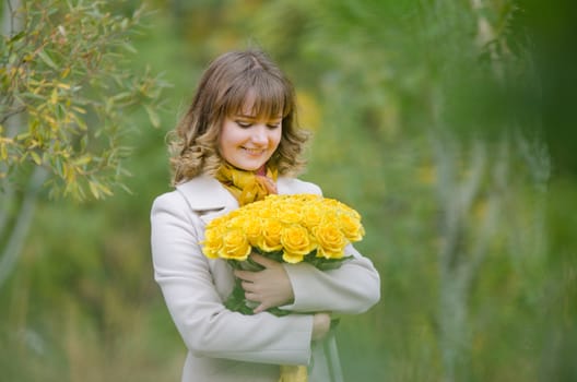Young cute girl with a bouquet of yellow roses in autumn cool weather