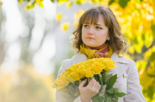 Young cute girl with a bouquet of yellow roses in autumn cool weather