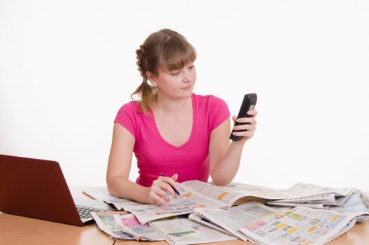 A young girl sits at a table with a pile of newspapers, encyclopedias and a laptop