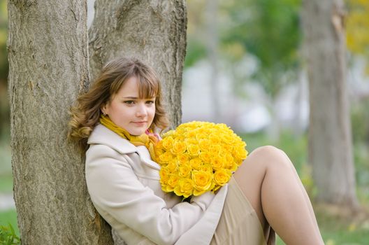 Young cute girl with a bouquet of yellow roses in autumn cool weather