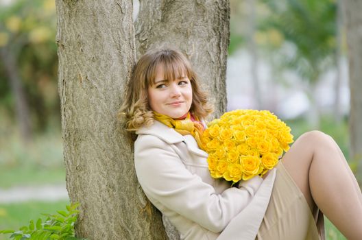 Young cute girl with a bouquet of yellow roses in autumn cool weather