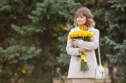 Young cute girl with a bouquet of yellow roses walks in autumn cool weather