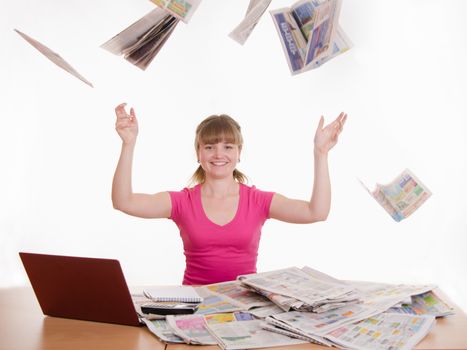 A young girl sits at a table with a pile of newspapers, encyclopedias and a laptop