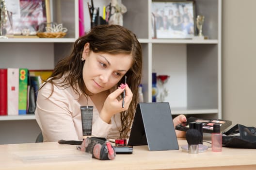 Young girl puts makeup in the office workplace